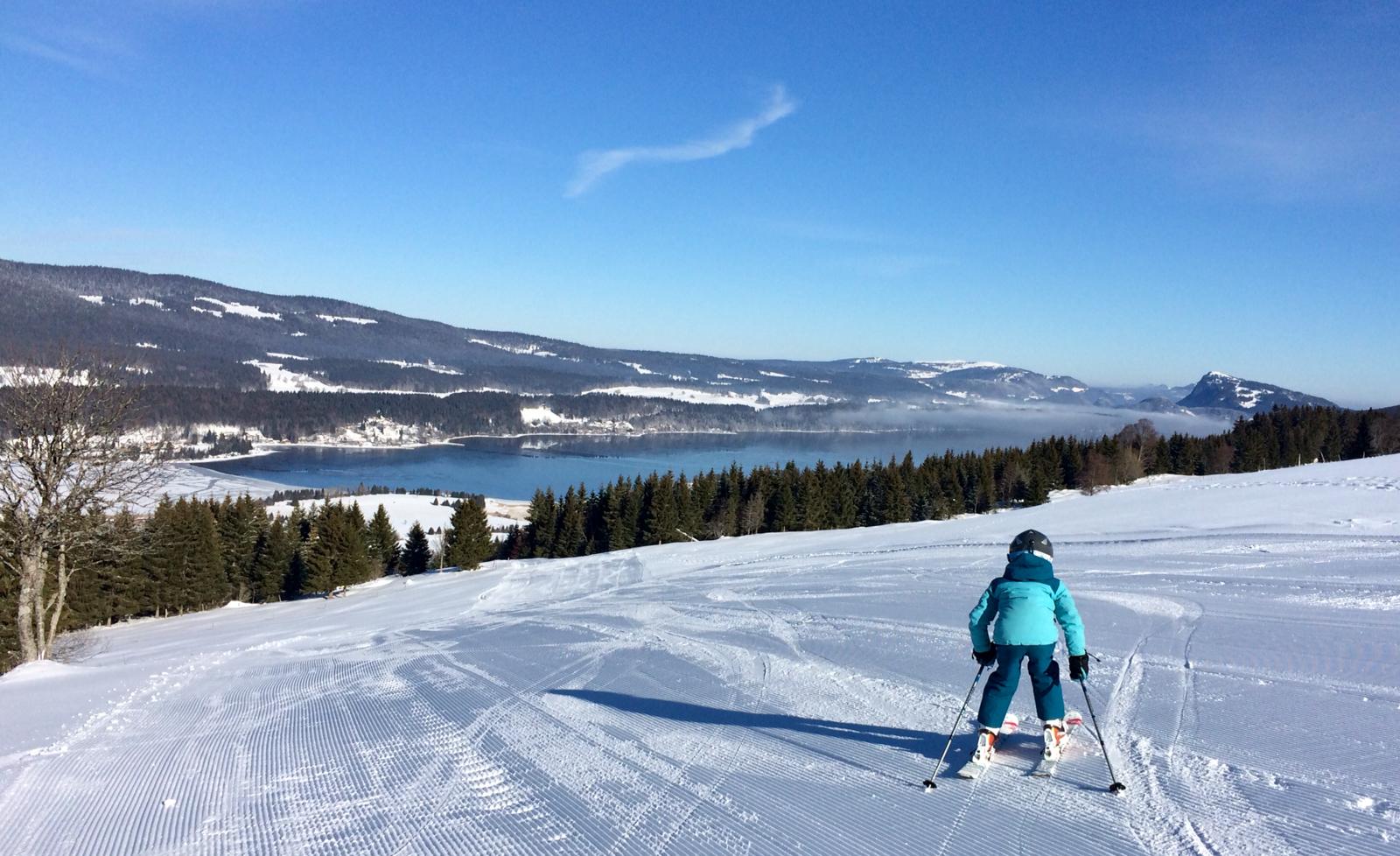 Jeune skieur dévalant les pistes de ski alpin de la Vallée de Joux, avec vue sur le lac de Joux.